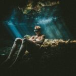 Travel to Mexico with Maritur DMC. A man sits on a rock in a cenote.